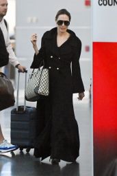 Angelina Jolie in a Chic Long Black Overcoat and Carrying a Dior Handbag at JFK Airport in New York 09/25/2023