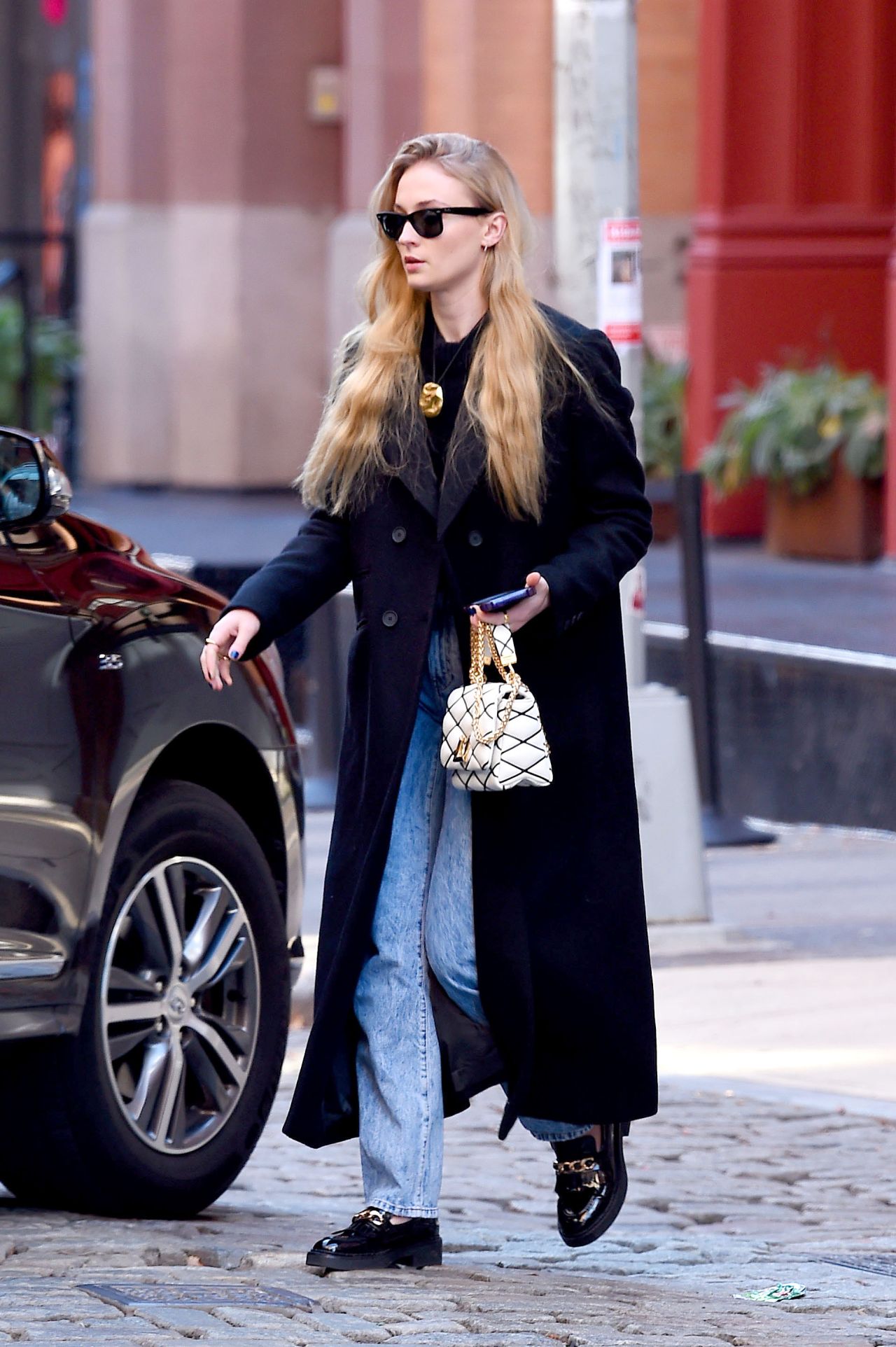 Sophie Turner in a Black Trench Coat, Matching Blouse, Jeans and Black ...