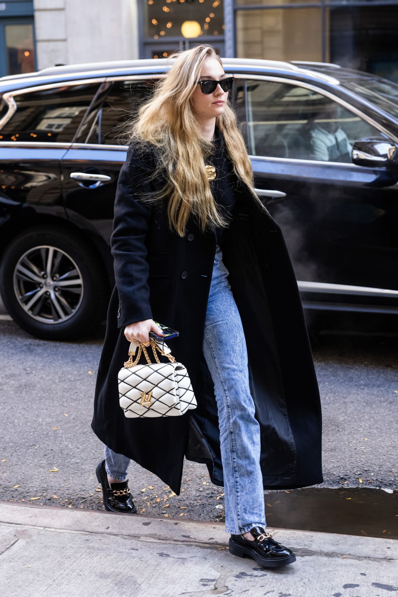 Sophie Turner in a Black Trench Coat, Matching Blouse, Jeans and Black ...