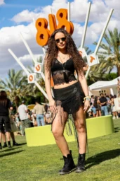 Madison Pettis posing in a black lace top and fringed skirt with lace-up boots at the 818 Outpost in Indio, CA, April 2026