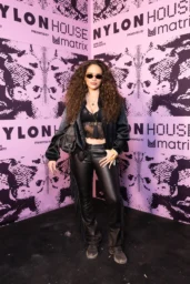 Madison Pettis posing in an all-black outfit with a satin bomber jacket and fringe leather pants at NYLON House in Thermal, April 2026