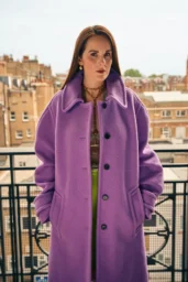 Michelle Dockery posing in a bold purple coat with gold jewelry for British Airways High Life Magazine photoshoot, September 2025