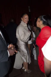 Rihanna smiling at a party in New York wearing a tan bomber jacket and silver satin skirt in April 2026