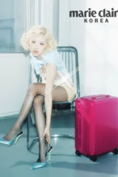 Rosé posing in a sequin mini dress with baby-blue scarf and blue slingbacks beside a pink Rimowa trunk for Marie Claire Korea photoshoot, April 2026