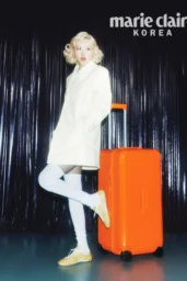 Rosé posing in a white coat with ribbed knee socks and beige sneakers beside an orange Rimowa suitcase for Marie Claire Korea photoshoot, April 2026