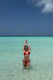 Demi Lovato in a red string bikini and black sunglasses beside clear turquoise water in August 2026